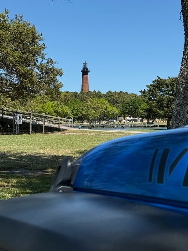 The red brick Currituck Beach Lighthouse in Corolla seen over the hood of a blue rental Jeep.