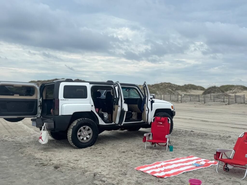 A silver Hummer H3 parked on the sand with its doors open, a picnic blanket and folding chairs set up beside it.