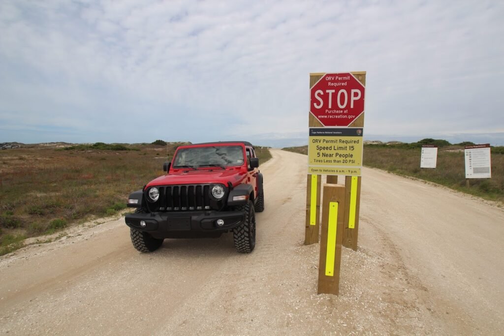A black Jeep Wrangler waiting at the stop sign and information kiosk at the entrance to a Cape Hatteras beach access ramp.