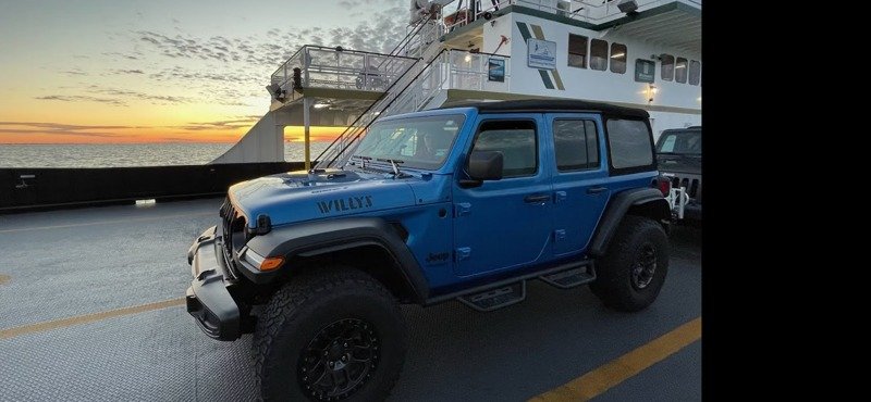 A blue Jeep Wrangler parked on the deck of the Hatteras–Ocracoke ferry at sunrise.
