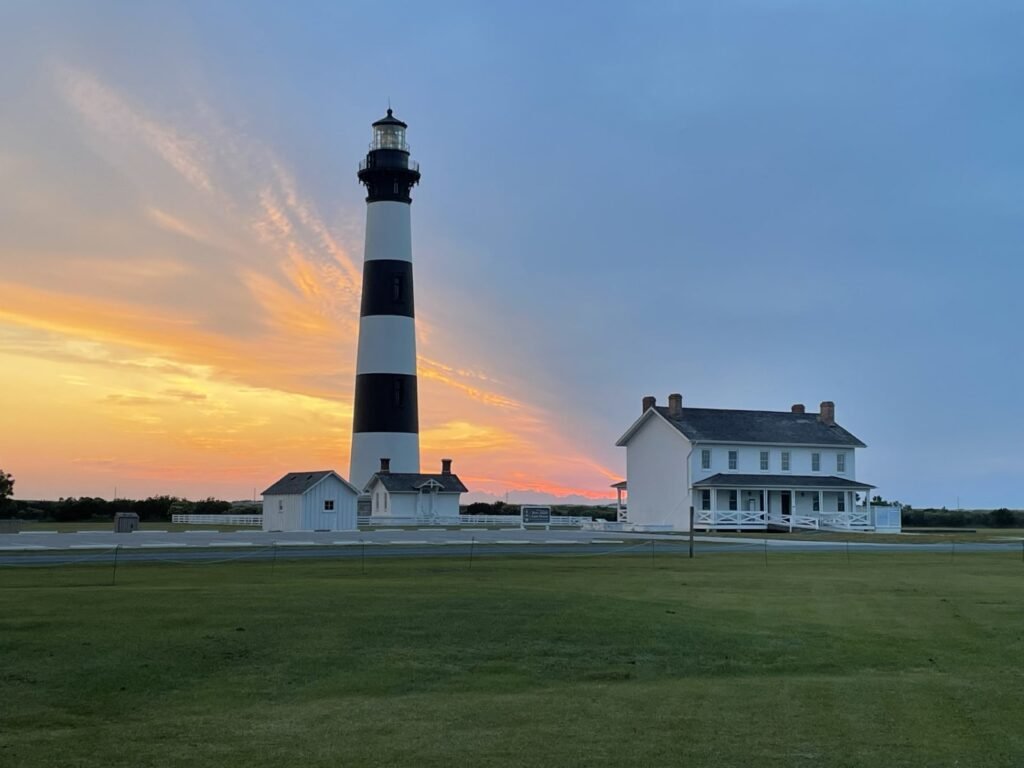 The black and white banded Bodie Island Lighthouse and its keepers' quarters lit by an orange sunrise near Nags Head.