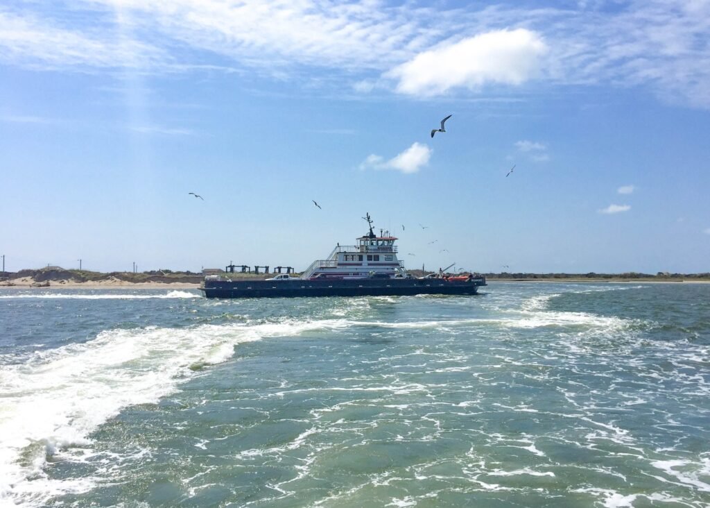Gulls trail the wake of the Hatteras–Ocracoke ferry as it crosses the inlet on a bright day.