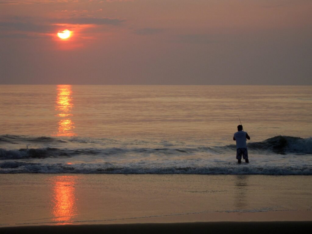 A lone angler stands in the morning surf silhouetted against an orange sunrise at Cape Hatteras National Seashore.