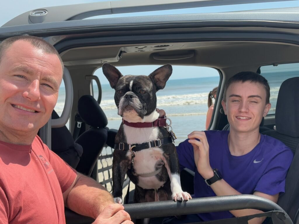 Two people and a small dog sitting together in the front of a rental four-wheel-drive.