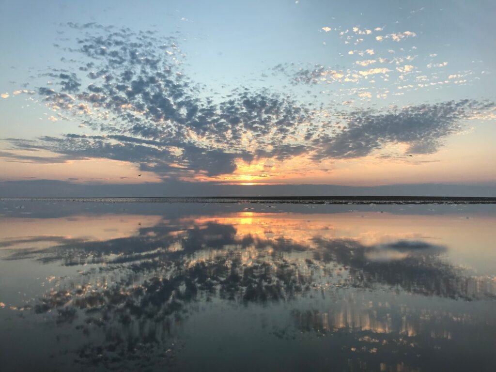 A patterned sky reflects in the still, shallow sound water south of Ramp 55 at sunrise.