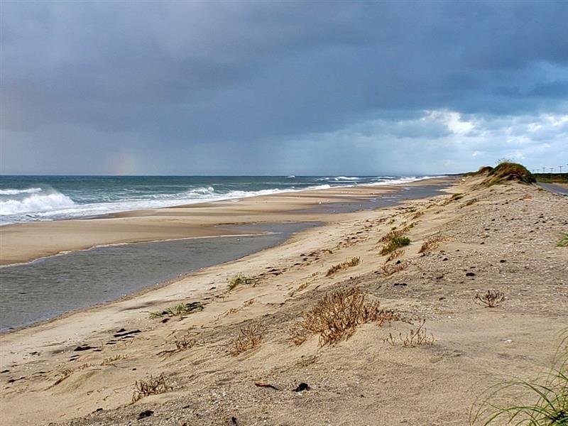 Standing water pools in the backshore behind the beach north of Ramp 63 after a high swell, with dunes on one side and surf on the other.